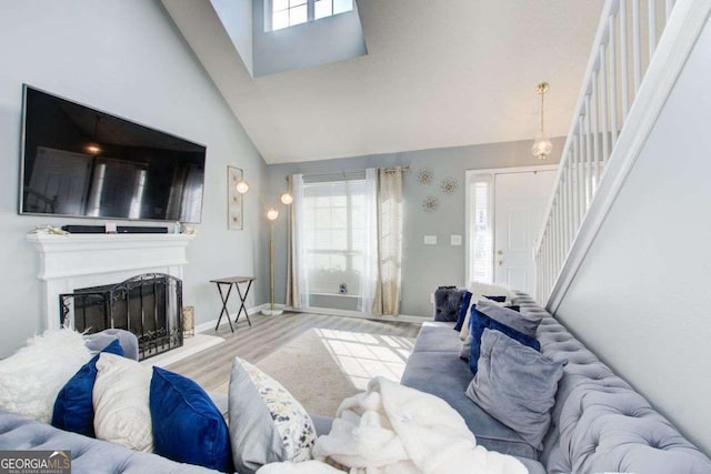 living area featuring light wood finished floors, stairway, a fireplace with raised hearth, and a wealth of natural light