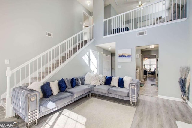 living room featuring stairs, visible vents, baseboards, and wood finished floors