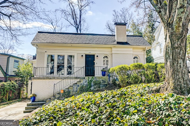 bungalow-style house with roof with shingles, a chimney, stairway, and brick siding