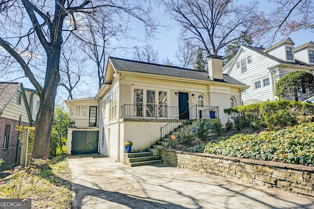 view of front of home featuring brick siding, roof with shingles, a chimney, driveway, and stairs