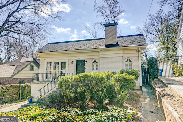 view of front of home featuring a chimney, roof with shingles, a gate, fence, and brick siding