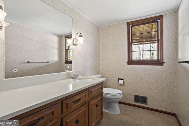 bathroom featuring toilet, vanity, baseboards, visible vents, and wallpapered walls