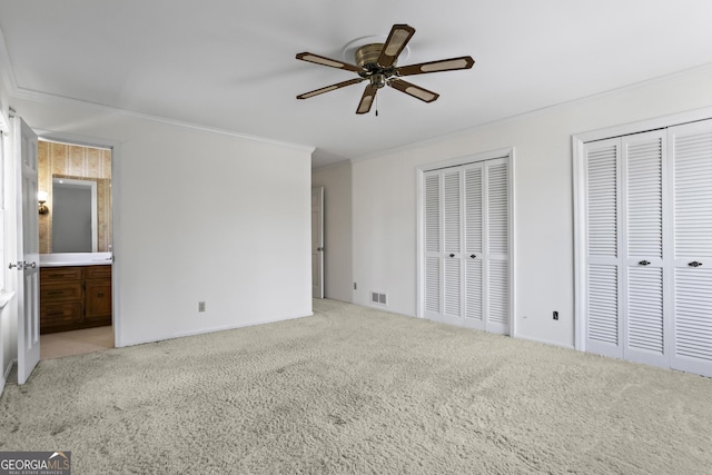 unfurnished bedroom with carpet floors, visible vents, two closets, and ornamental molding