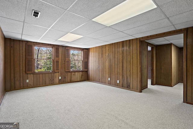 unfurnished room featuring baseboards, light carpet, wood walls, and a drop ceiling