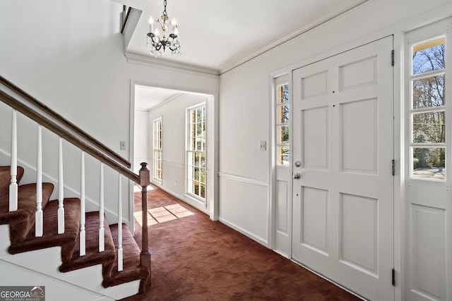 entrance foyer with plenty of natural light, stairway, ornamental molding, dark colored carpet, and a notable chandelier