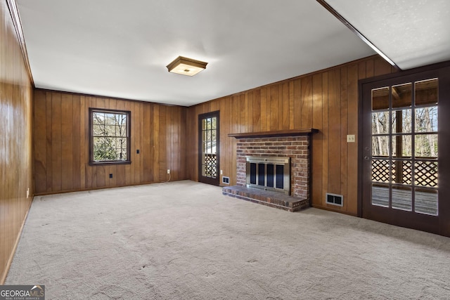 unfurnished living room featuring light carpet, a brick fireplace, visible vents, and wood walls