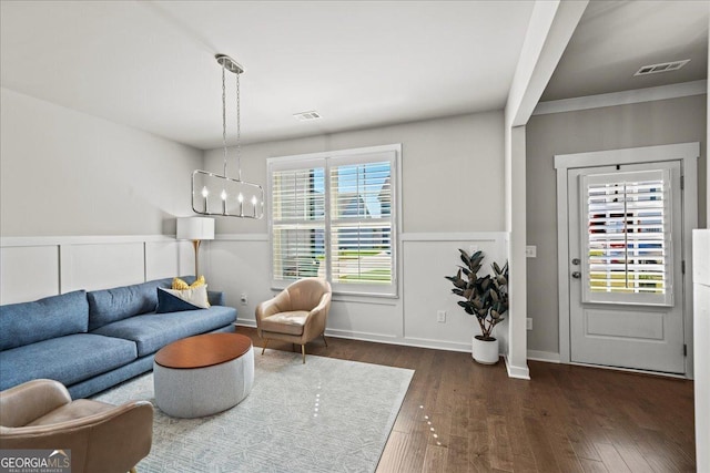 living area with dark wood-type flooring, an inviting chandelier, wainscoting, and visible vents