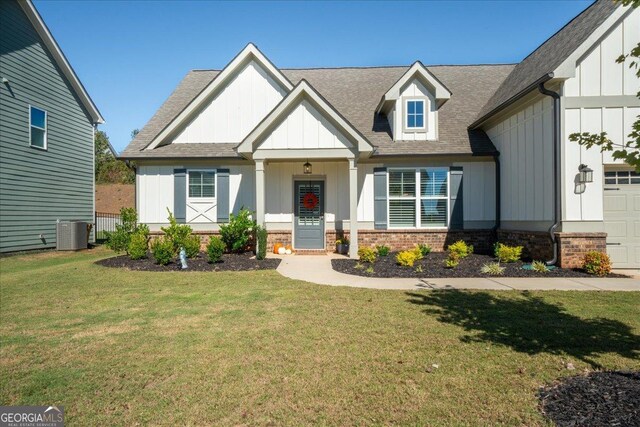 view of front of home with board and batten siding, a front yard, brick siding, a shingled roof, and central AC unit