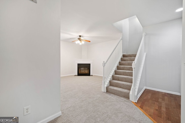 stairway featuring carpet floors, a fireplace with flush hearth, baseboards, and ceiling fan