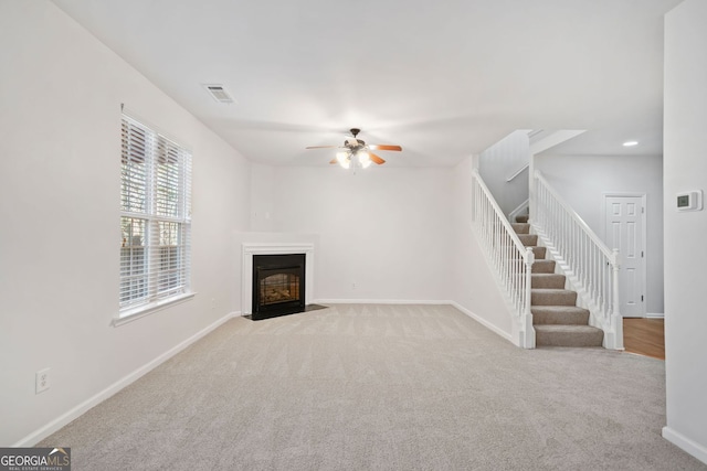 unfurnished living room with visible vents, a fireplace with flush hearth, light carpet, baseboards, and stairs