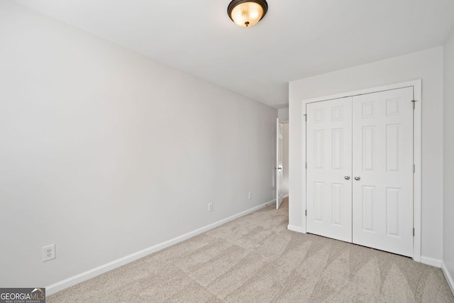 unfurnished bedroom with a closet, light carpet, and baseboards