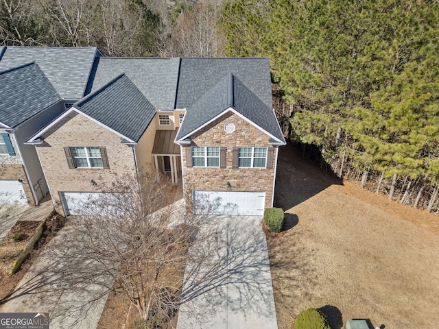 view of front of home with driveway, stone siding, roof with shingles, and an attached garage