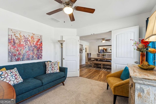 carpeted living area featuring ceiling fan, wood finished floors, and visible vents