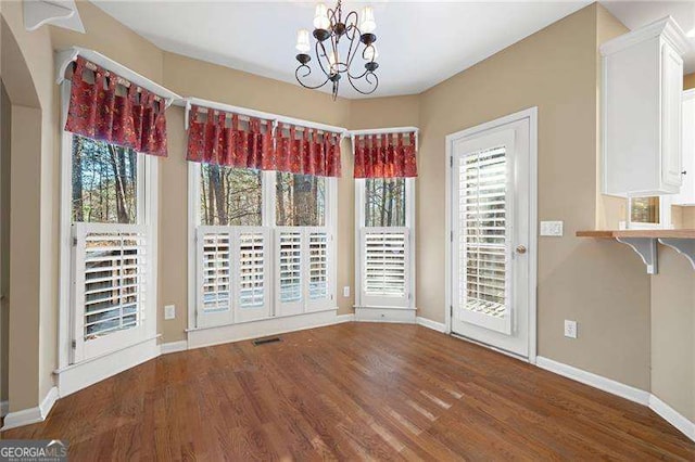 unfurnished dining area featuring wood finished floors, a wealth of natural light, and a notable chandelier