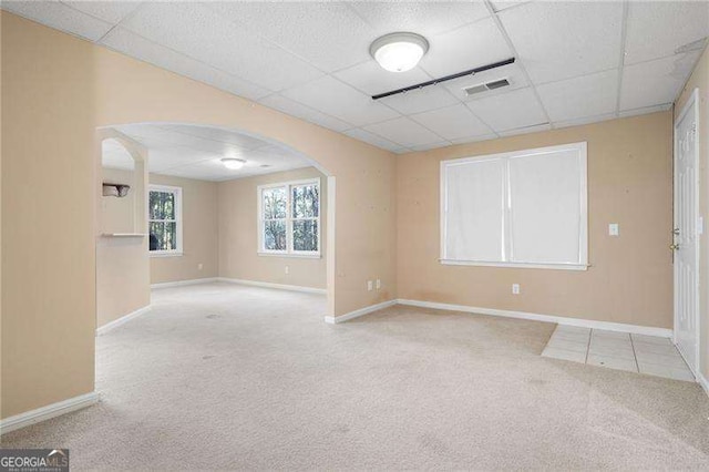 unfurnished room with light carpet, baseboards, arched walkways, visible vents, and a paneled ceiling