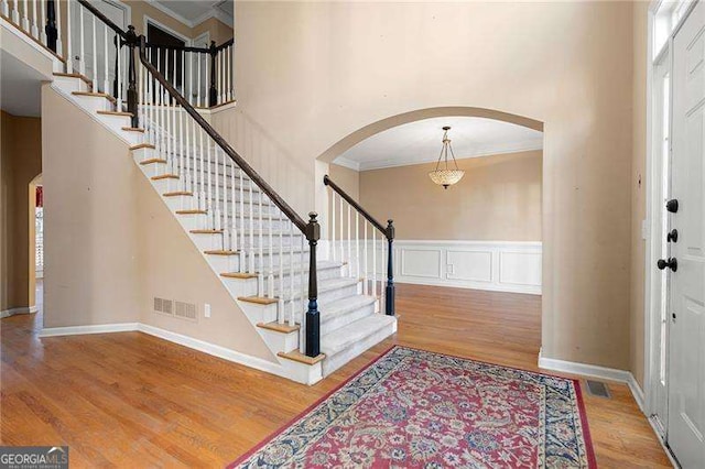 entryway with wood finished floors, a towering ceiling, and crown molding