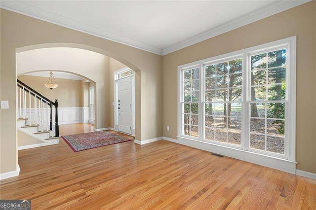 entryway with light wood-style flooring, arched walkways, ornamental molding, and stairway