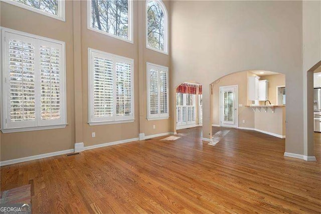 unfurnished living room with a healthy amount of sunlight, baseboards, arched walkways, and wood finished floors