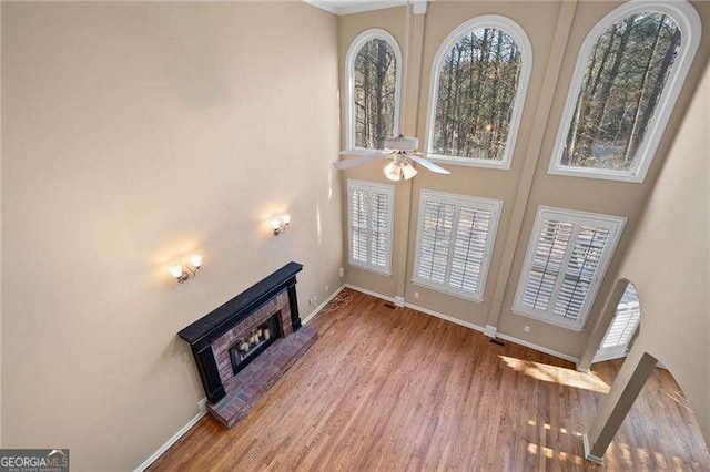 living room featuring ceiling fan, a fireplace, baseboards, and wood finished floors