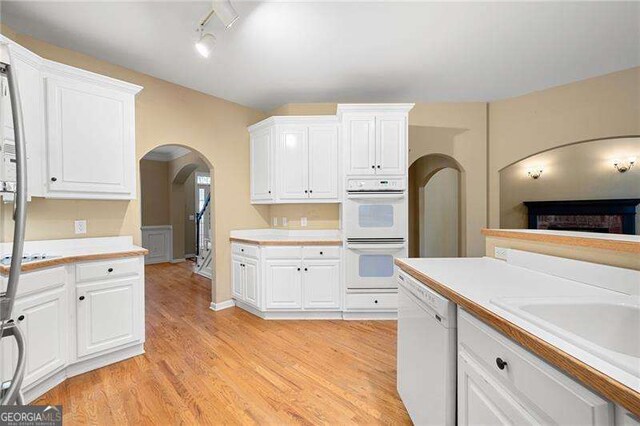 kitchen with arched walkways, light countertops, white appliances, and white cabinets