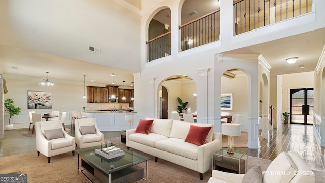 living room featuring arched walkways, ornamental molding, wood finished floors, and visible vents