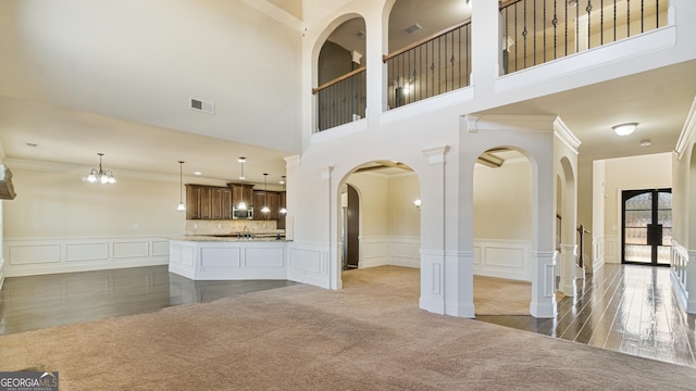 unfurnished living room featuring arched walkways, a decorative wall, visible vents, carpet, and crown molding