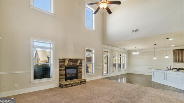 unfurnished living room with ceiling fan with notable chandelier, a fireplace, visible vents, ornamental molding, and dark carpet