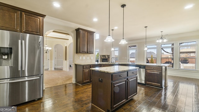 kitchen with arched walkways, stainless steel appliances, a peninsula, a sink, and dark brown cabinets