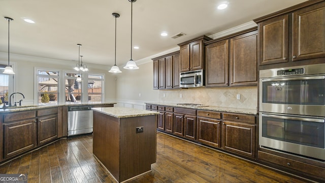 kitchen featuring stainless steel appliances, a sink, visible vents, ornamental molding, and a center island