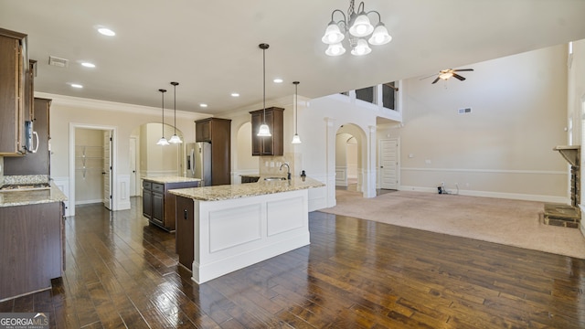 kitchen with arched walkways, dark brown cabinetry, ceiling fan with notable chandelier, dark wood finished floors, and stainless steel fridge