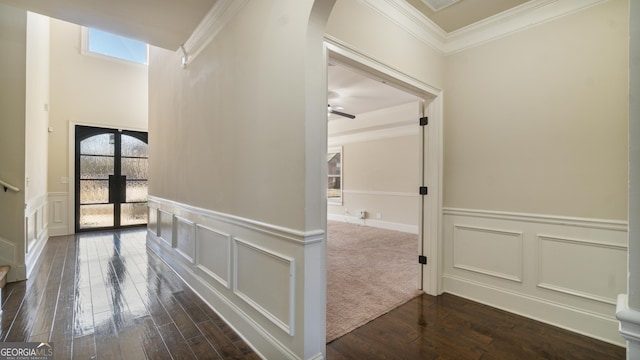 hall featuring crown molding, arched walkways, a decorative wall, and dark wood-type flooring