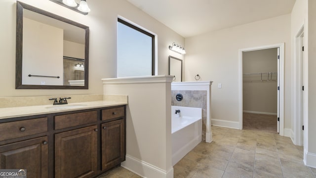 full bathroom featuring a spacious closet, a garden tub, vanity, and baseboards