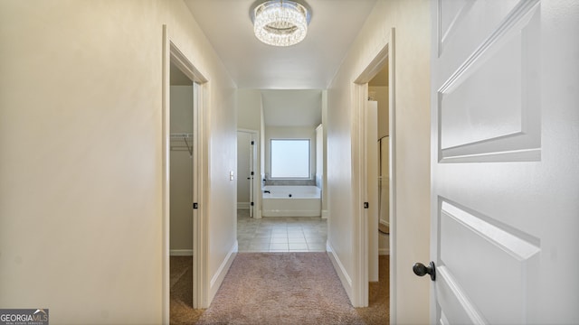 corridor featuring baseboards, carpet flooring, and an inviting chandelier