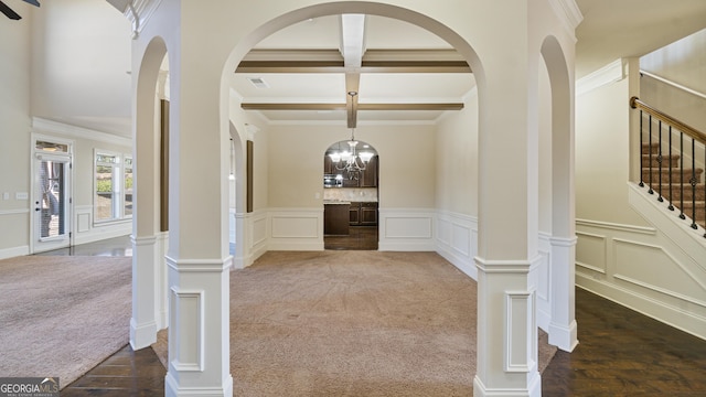 hallway with coffered ceiling, stairway, carpet flooring, a decorative wall, and beam ceiling