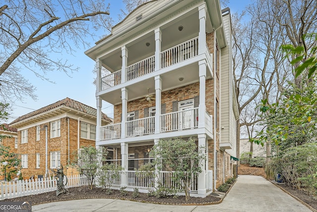 view of front facade featuring brick siding, ceiling fan, a balcony, and fence