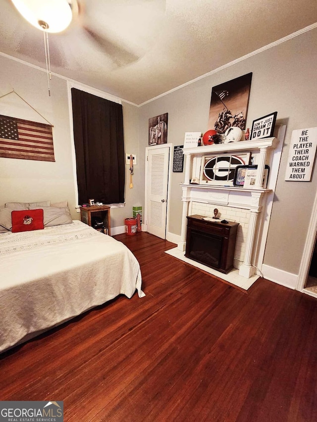 bedroom featuring wood finished floors, a ceiling fan, baseboards, a brick fireplace, and crown molding