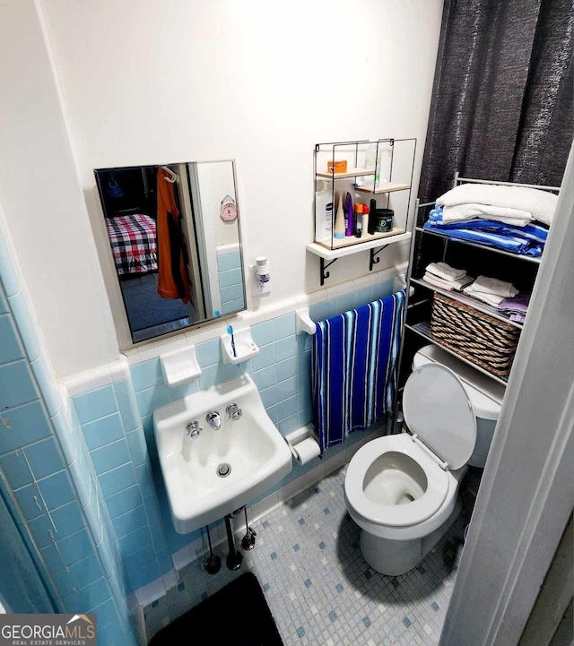 bathroom featuring tile walls, wainscoting, toilet, tile patterned flooring, and a sink