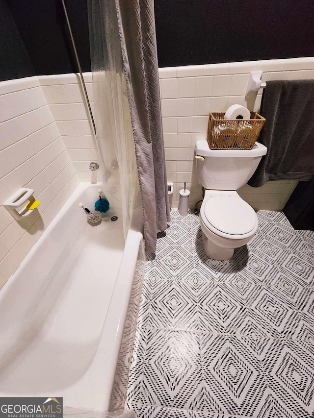 bathroom with tile walls, shower / bath combination with curtain, toilet, wainscoting, and tile patterned floors