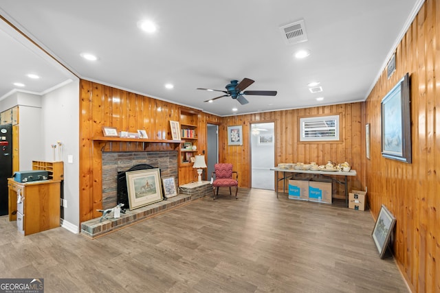 living room with wood walls, wood finished floors, visible vents, and crown molding