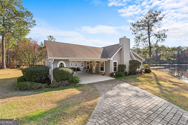 view of front of home with a shingled roof, a water view, a chimney, and a front lawn