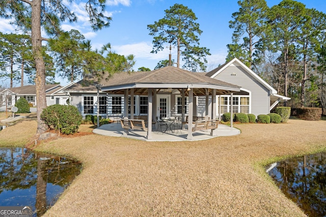 rear view of house with a shingled roof, a yard, and a patio