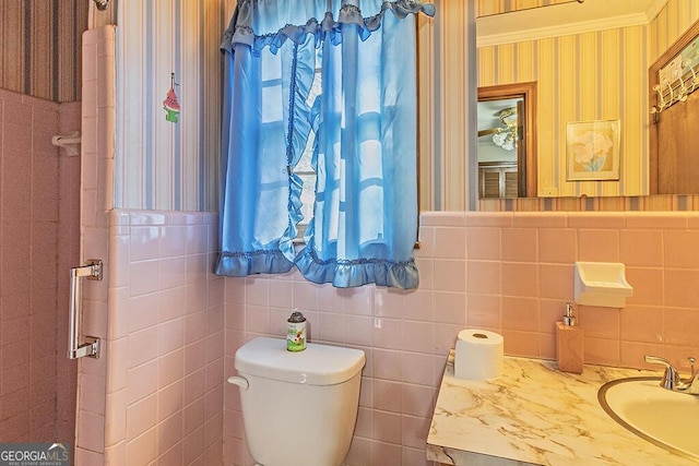 bathroom with a wainscoted wall, vanity, toilet, and wallpapered walls