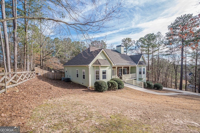 back of house featuring fence, a chimney, covered porch, central air condition unit, and a shingled roof