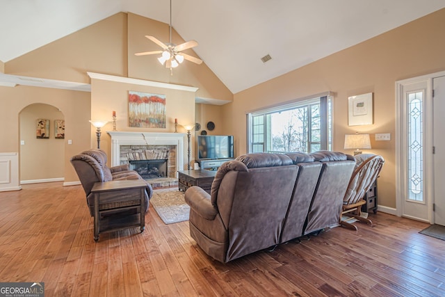 living area with visible vents, high vaulted ceiling, wood-type flooring, arched walkways, and a stone fireplace