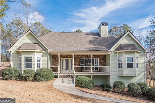 view of front facade featuring covered porch, roof with shingles, a chimney, and fence