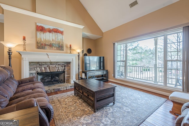 living area with high vaulted ceiling, visible vents, a stone fireplace, and wood finished floors