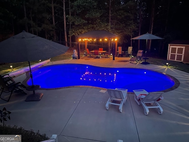 pool at night with a gazebo, an outdoor pool, an outbuilding, and a patio area