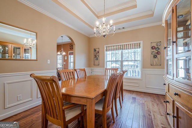 dining space with a tray ceiling, wainscoting, light wood-style floors, an inviting chandelier, and arched walkways