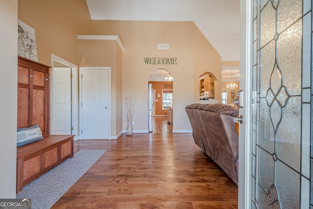 entryway with arched walkways, wood finished floors, a chandelier, baseboards, and a high ceiling