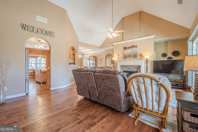 living room with a ceiling fan, a stone fireplace, arched walkways, wood-type flooring, and high vaulted ceiling
